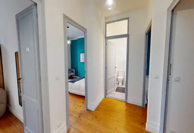 Corridoio luminoso e ben composto con ingressi verso una camera da letto e un bagno; pavimenti in legno lucido e cornici delle porte grigio chiaro donano un aspetto caldo ed elegante.