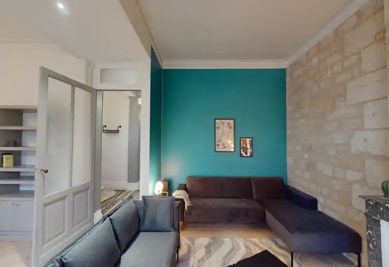 Soggiorno contemporaneo con parete d'accento turchese, divani a penisola, tappeto e parete in pietra a vista — ambiente luminoso, elegante e accogliente ideale per il relax.