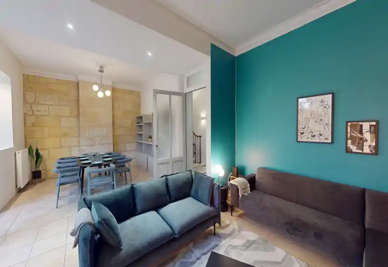 Zona giorno elegante e open-space con due divani comodi, tappeto decorato e una parete accent in tonalità turchese — perfetta per rilassarsi o ricevere ospiti.