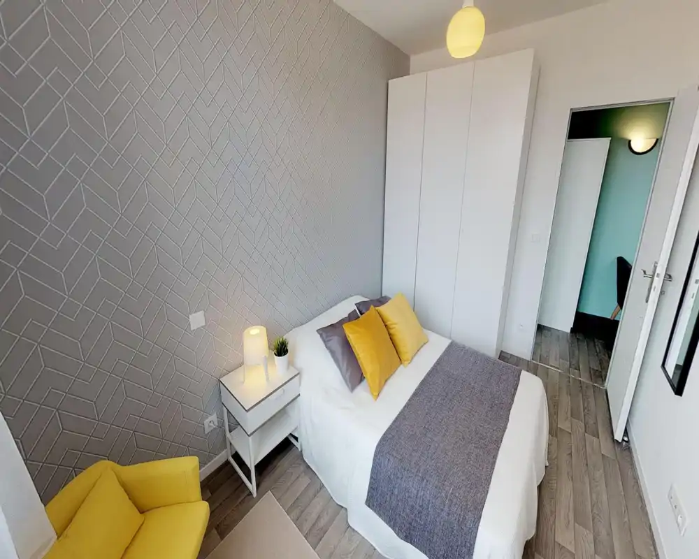 Bright, stylish bedroom with a double bed dressed in white linens, mustard accent pillows and a coordinating throw; a bedside table with lamp and a white wardrobe provide practical storage.