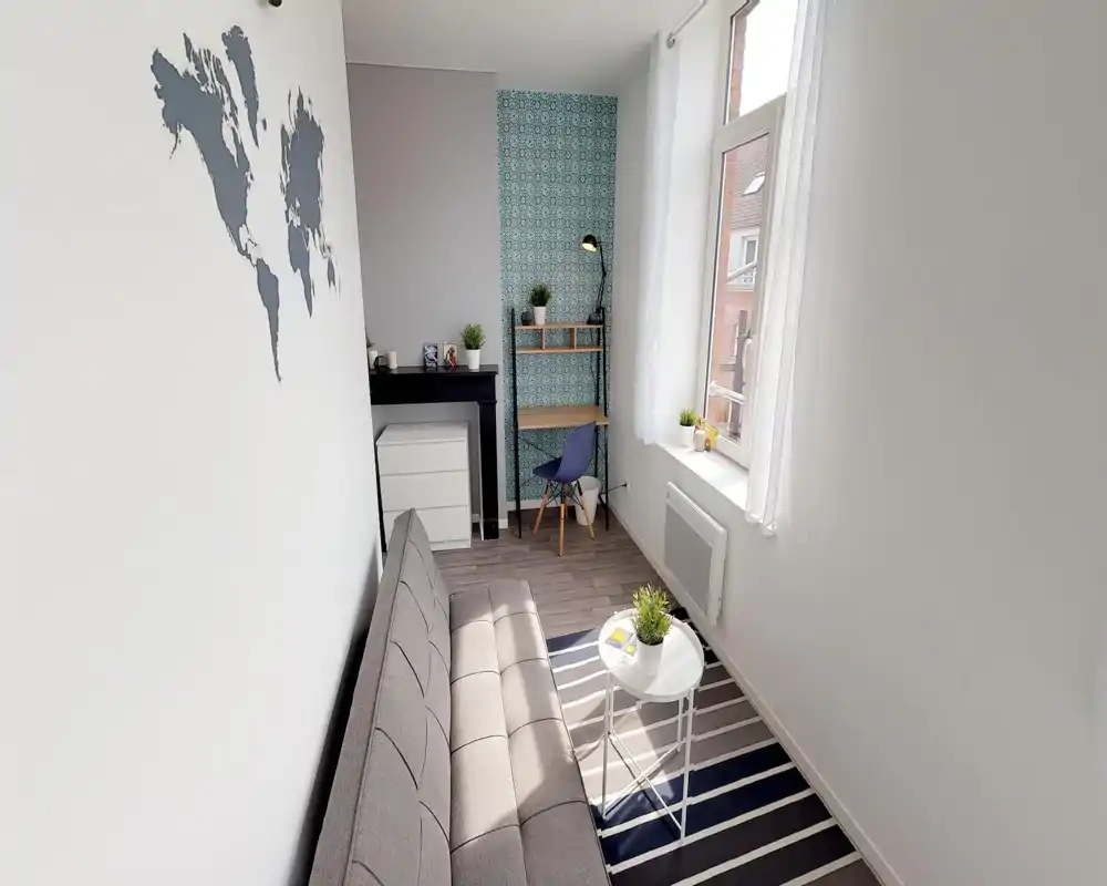 Espace de vie lumineux et compact avec un canapé gris, un tapis rayé et une petite table basse. Un bureau avec étagères et plantes décoratives sous un mur à motif le rend adapté à la détente et au travail.