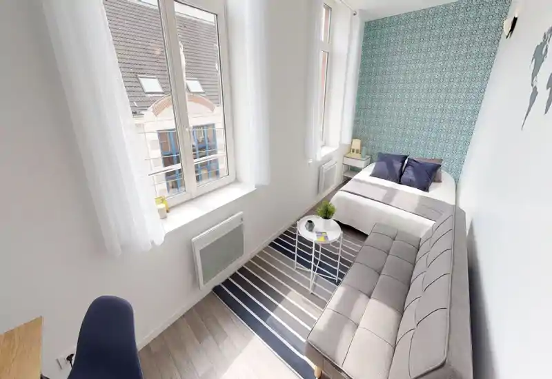 Chambre lumineuse et bien décorée avec lit double contre un mur à motif, petit canapé et tapis rayé; de grandes fenêtres apportent une belle lumière naturelle.
