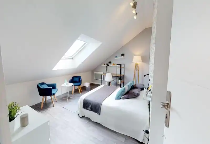 Bright, stylish attic bedroom with a skylight, double bed with crisp linens, bedside lamp and a small seating area — perfect for a cozy stay.