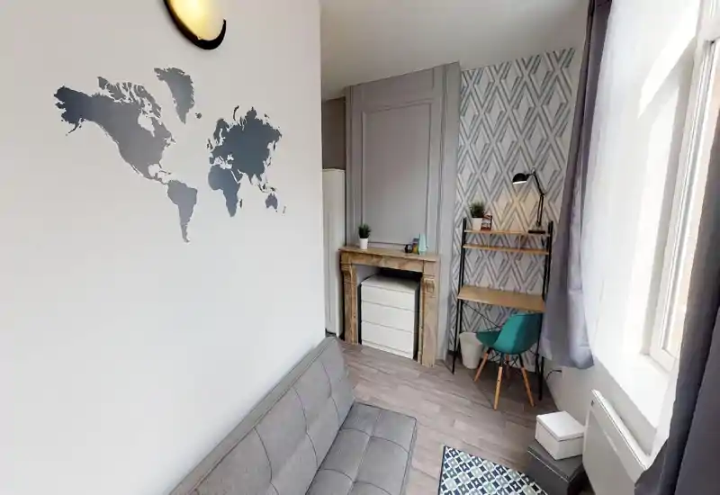Petit salon moderne et lumineux avec canapé gris, tapis à motifs et bureau compact près de la fenêtre ; sticker mural et plantes apportent du caractère.