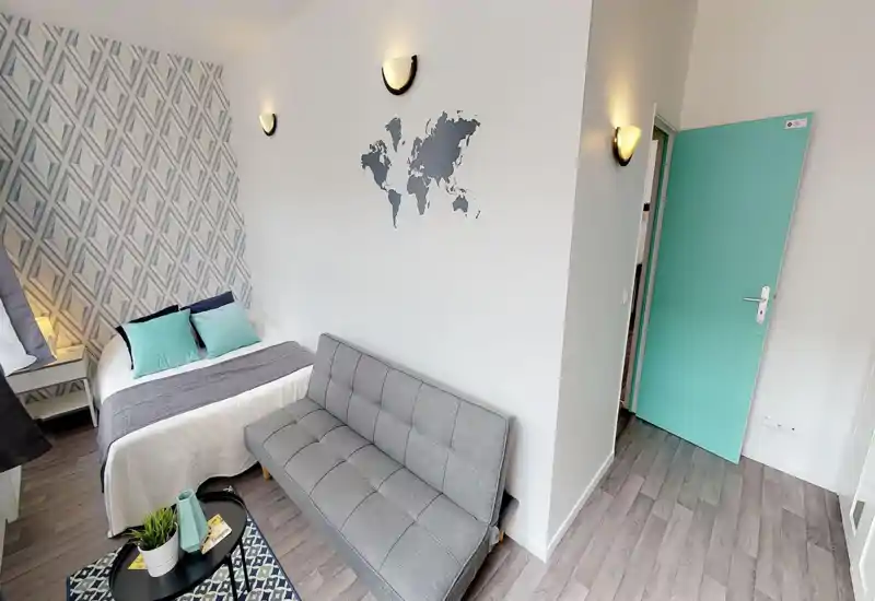 Chambre lumineuse et bien aménagée avec un lit double complet, des coussins décoratifs et un petit canapé gris; papier peint moderne et touches vert menthe pour une ambiance fraîche et cosy.