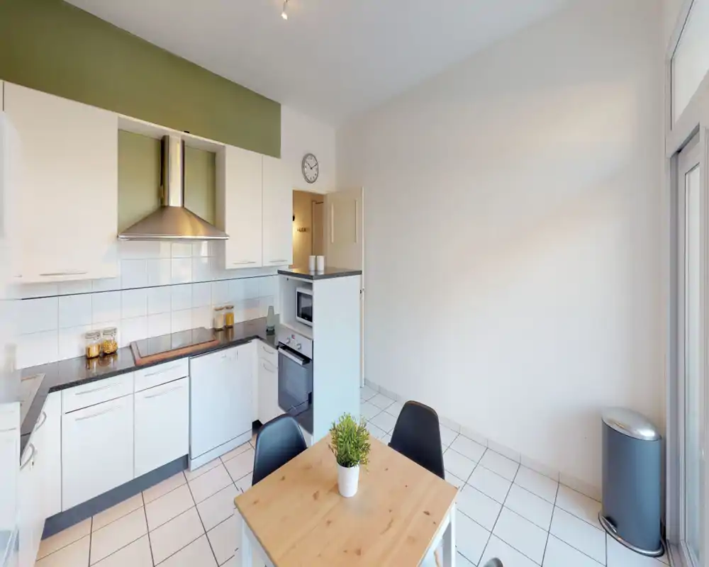 Bright, modern kitchen with white cabinets, a stainless steel hood, built-in oven and dishwasher, and a small dining table with plant—clean and functional layout ideal for everyday cooking.