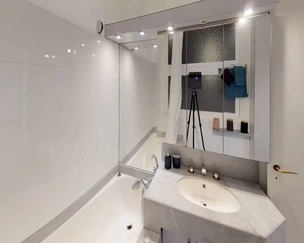 Modern bathroom with a built-in bathtub, marble-effect countertop and sink, mirrored cabinets and recessed ceiling lights; clean, bright and well maintained.