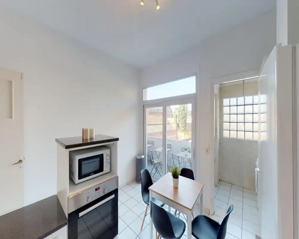 Bright, compact kitchen with built-in oven, microwave and a small dining table. Large glass doors open onto a balcony, offering good natural light and outdoor access.