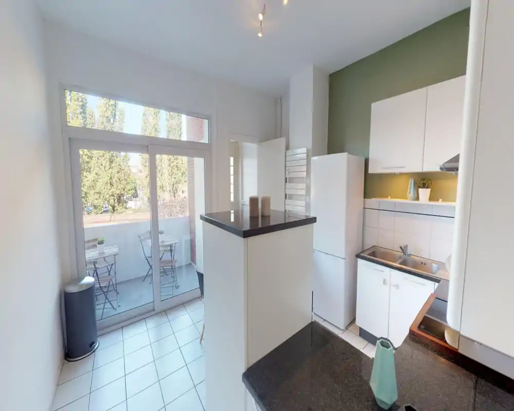 Bright modern kitchen with white cabinets, a sink and fridge, plus a small island and large sliding doors leading to a balcony — ideal for morning light.