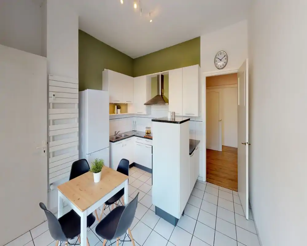 Modern compact kitchen with white cabinets, black countertops and a small dining table for four; bright, tidy and functional layout ideal for city apartments.