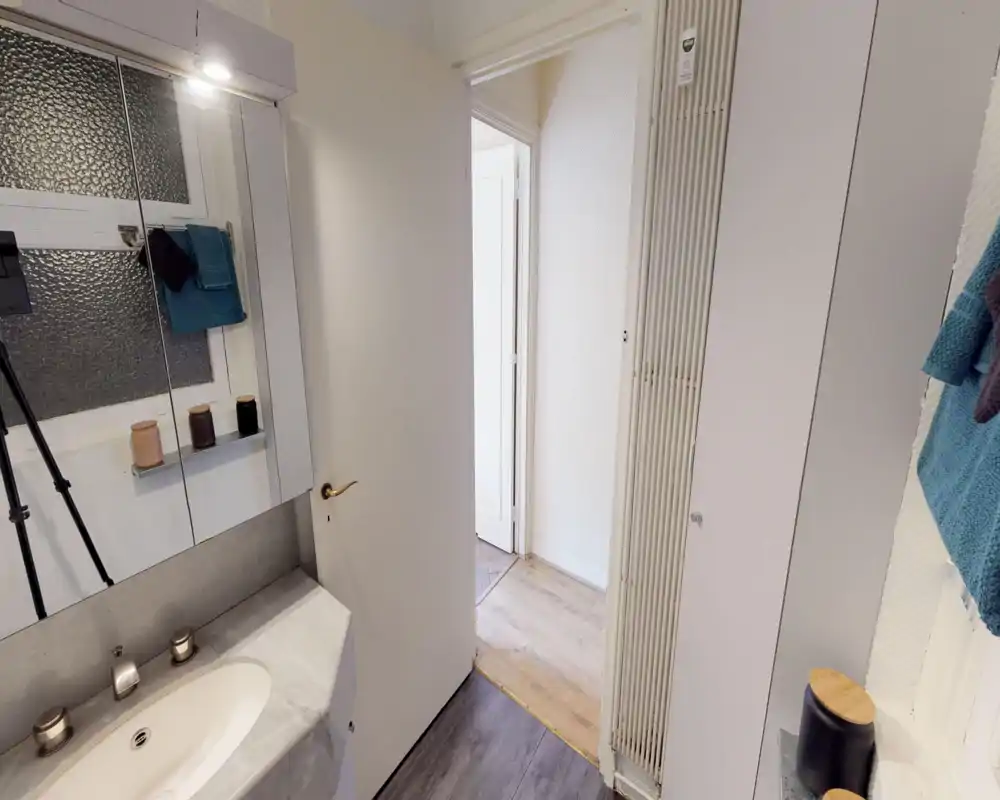 Small, well-lit bathroom corner with a marble sink, mirrored cabinet and towel hooks, shown clearly for listing photos.