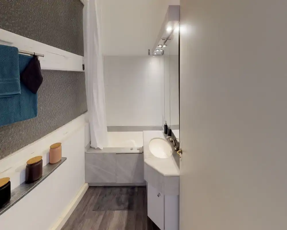 Modern bathroom with a bathtub, marble-effect sink countertop and large mirror. Neutral tones and good lighting create a clean, functional space.