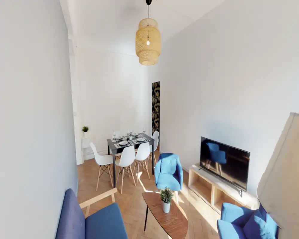 Bright, stylish living room with blue upholstered seating, a low wooden coffee table and a TV unit; a dining table with white chairs is visible, making this an inviting combined living and dining space.