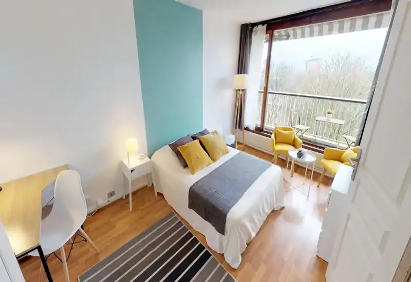 Bright, well-staged bedroom with a double bed, cozy textiles and a large window opening onto a balcony — perfect for relaxing or working by natural light.