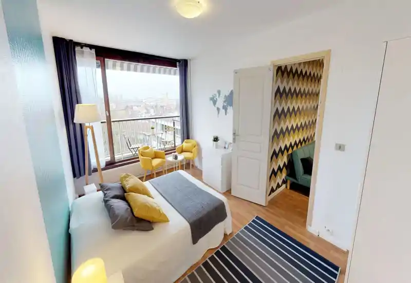 Bright, stylish bedroom with a double bed, coordinated cushions and a cosy throw; large window and small balcony with seating add natural light and a pleasant view.
