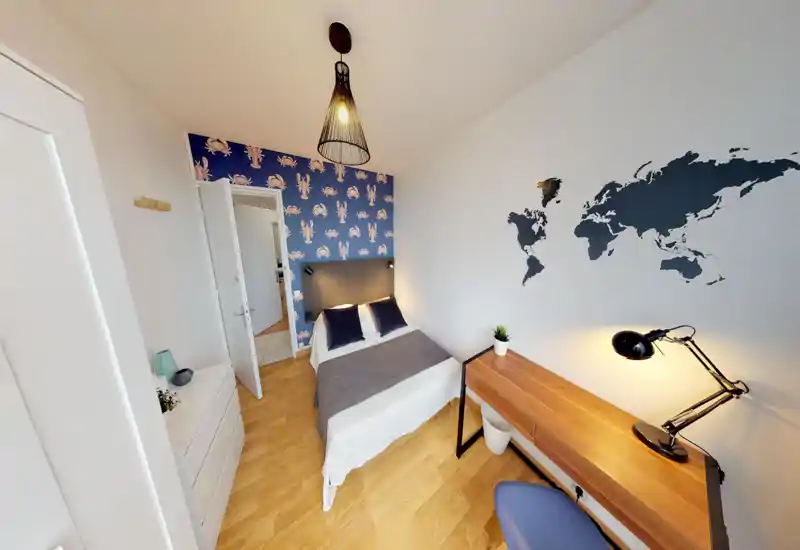 Chambre lumineuse et bien mise en scène avec lit double, papier peint bleu derrière la tête de lit et bureau en bois avec lampe — un espace moderne et confortable, idéal pour de courts séjours.