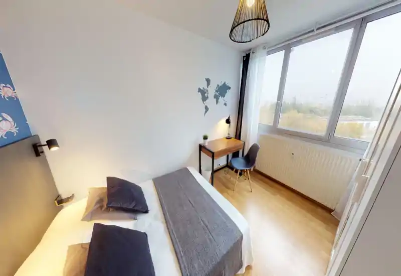 Chambre moderne et lumineuse avec grande fenêtre, lit double en linge neutre et petit bureau en bois près de la fenêtre — idéale pour se reposer et travailler à la lumière du jour.