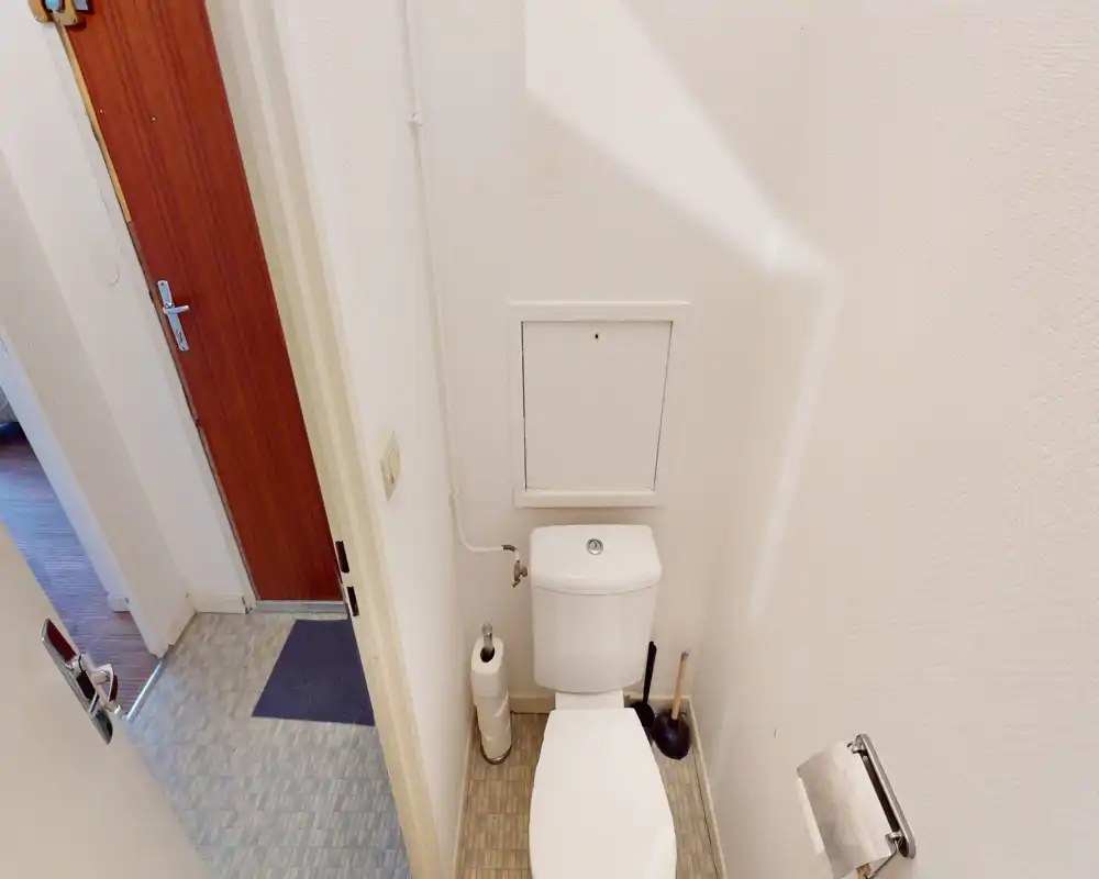 Small, clean WC with a close-up view of the toilet, toilet brush and roll holder; tiled floor and a white wall-mounted access panel.
