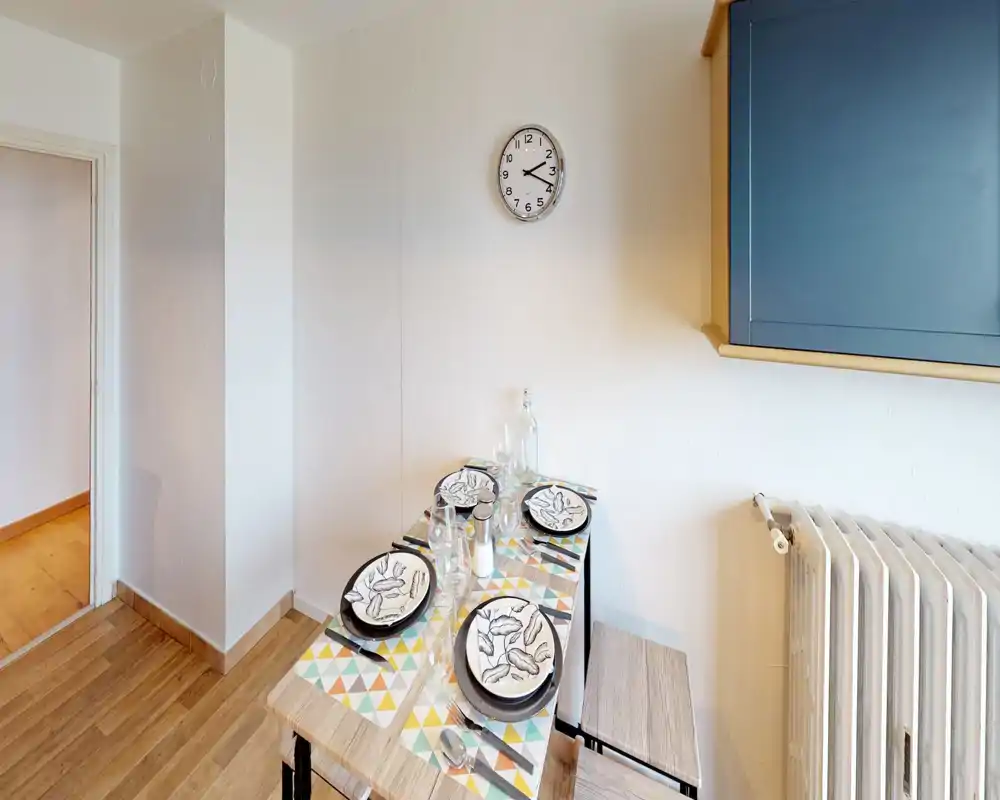 Coin repas compact et lumineux dressé pour quatre personnes, avec sets de table à motifs et tabourets en bois — idéal pour des repas décontractés en appartement.