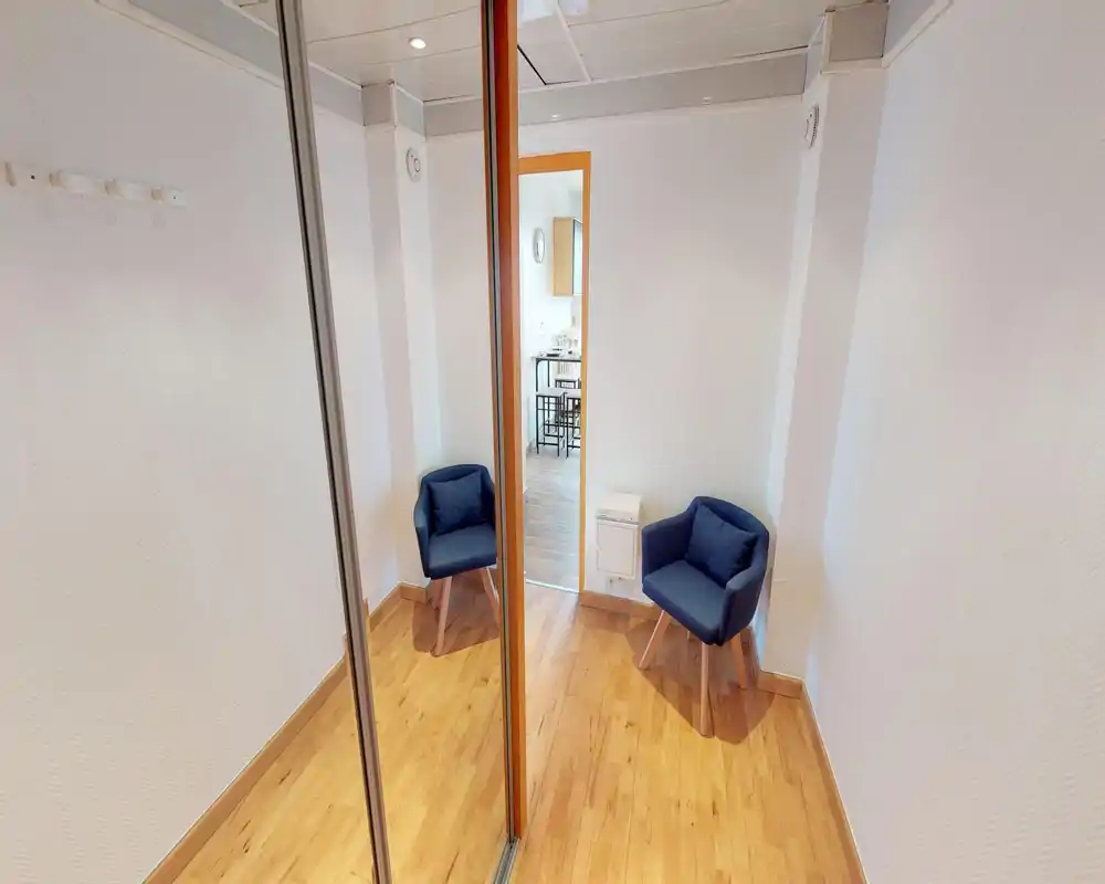 Petit coin salon avec deux fauteuils bleu marine sur un sol en bois chaleureux ; murs clairs et penderie miroir qui agrandit visuellement l'espace.