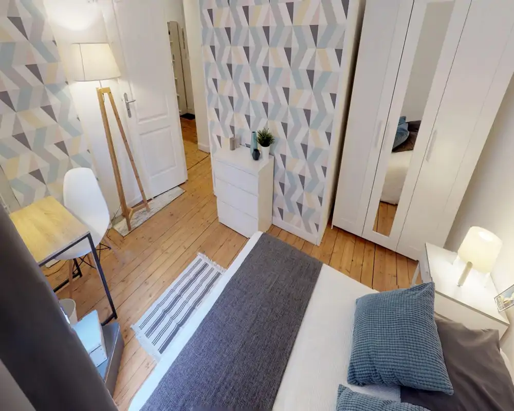 Camera da letto luminosa e curata con un letto matrimoniale in primo piano, cuscini decorativi, pavimento in legno e un armadio bianco con anta a specchio — ambiente accogliente e ben illuminato, ideale per annunci.