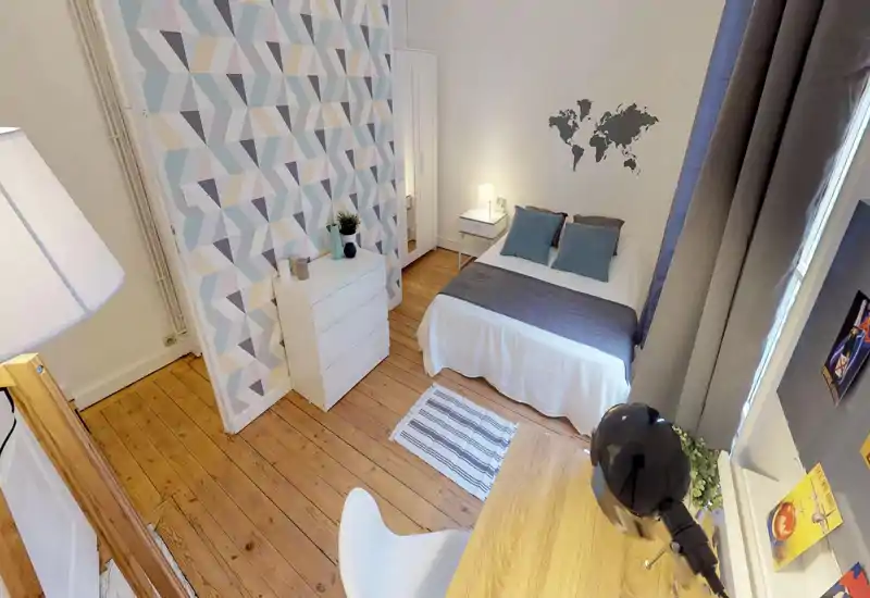 Camera da letto luminosa e ordinata con letto matrimoniale, comodino e cuscini decorativi; parete con motivo geometrico e pavimento in legno conferiscono calore.