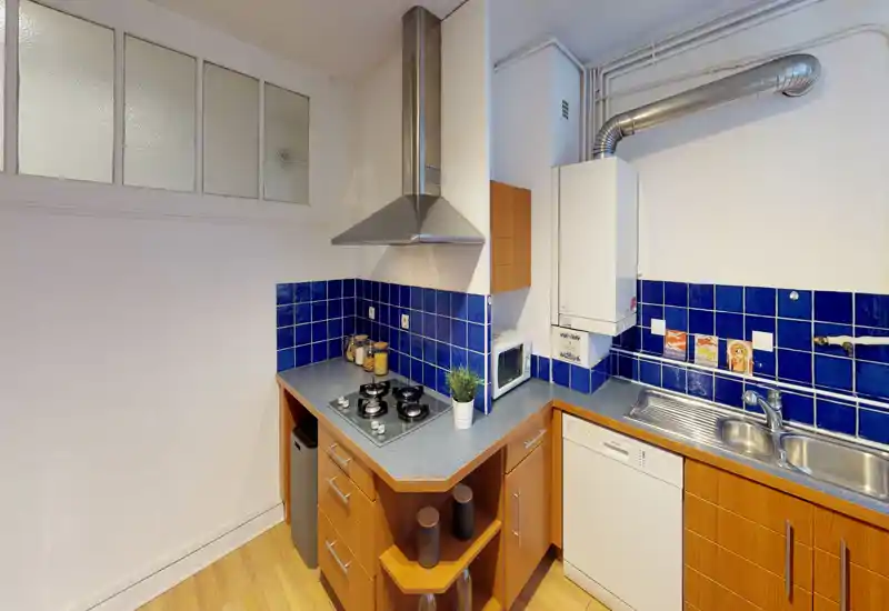 Cucina compatta con paraschizzi in piastrelle blu, piano cottura a gas incassato, lavello in acciaio inox e mobili in legno — luminosa e ben organizzata per un appartamento cittadino.