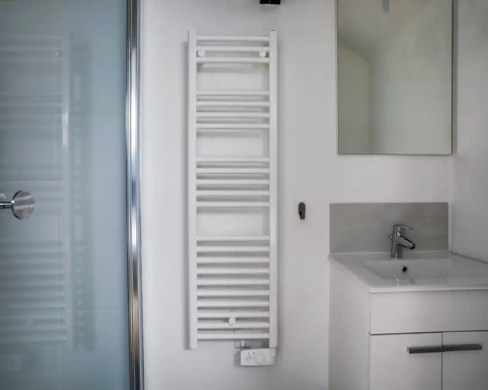 Angolo bagno moderno e pulito con termoarredo bianco, lavabo con rubinetto cromato e specchio — luminoso, minimal e ben tenuto.