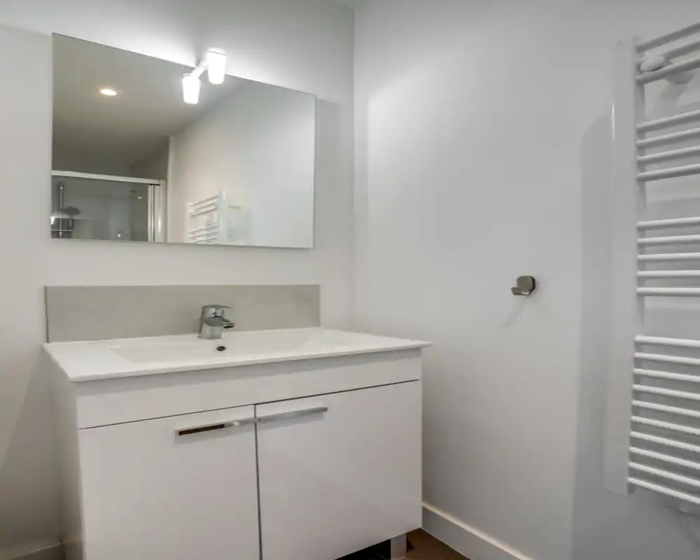 Coin lavabo de salle de bain moderne et compact avec miroir mural, mitigeur monocommande et radiateur-serviettes; lumineux, minimaliste et soigné.
