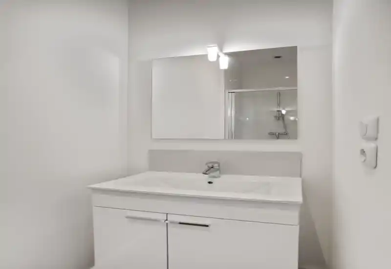 Compact modern bathroom vanity with a white sink, chrome faucet and a mirrored cabinet above; clean minimalist styling and bright lighting.