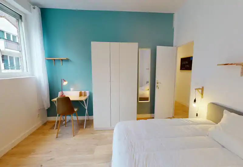 Bright, modern bedroom with a comfortable double bed, teal accent wall, wardrobe and a small desk by the window — ideal for work and relaxation.
