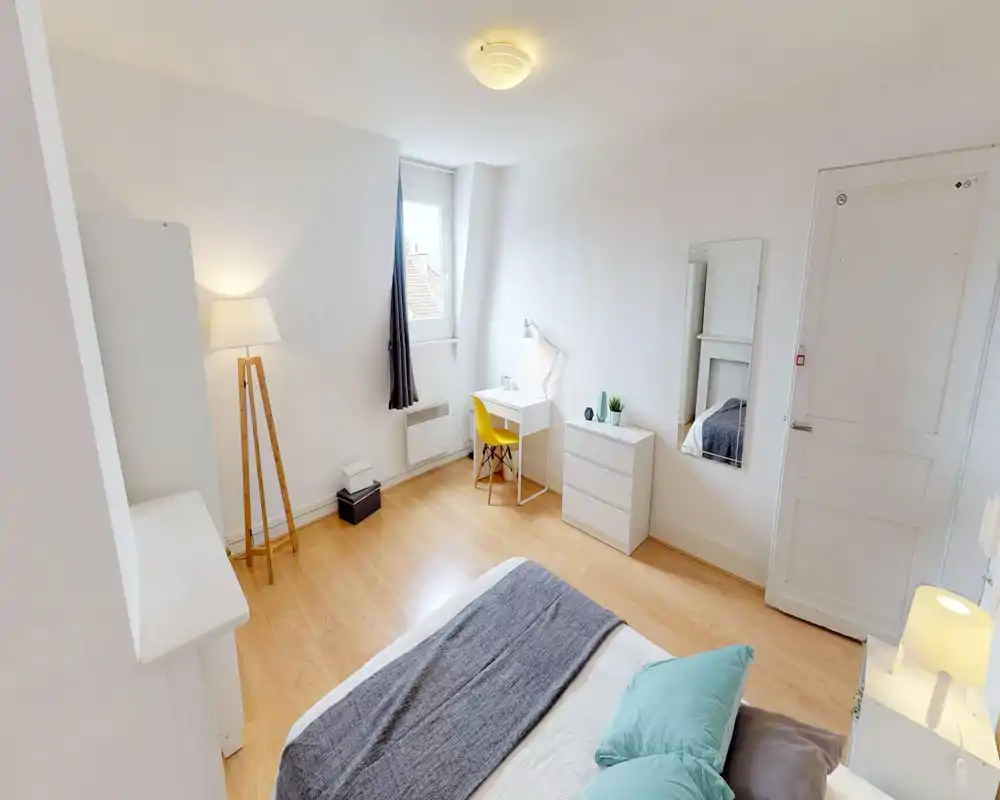 Chambre lumineuse et minimaliste avec un grand lit au premier plan, textiles doux et un bureau près de la fenêtre. Palette neutre et sol en bois pour une ambiance calme et aérée, idéale pour les annonces.
