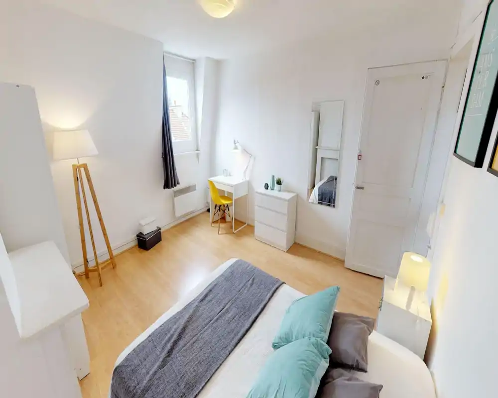 Chambre lumineuse et moderne avec un grand lit au premier plan, coussins moelleux et palette neutre. Un bureau près de la fenêtre et une grande glace complètent l'aménagement fonctionnel.