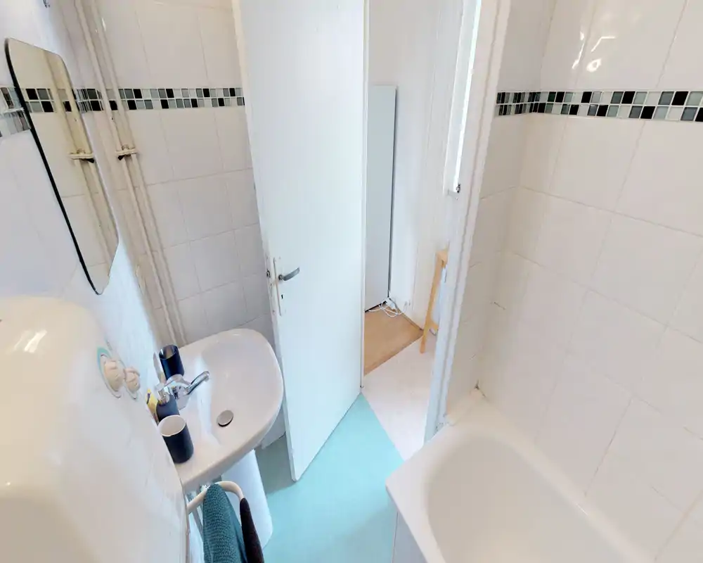 Compact tiled bathroom with a pedestal sink, bathtub, small mirror and tidy accessories; bright, clean and functional space ideal for a short-stay rental.