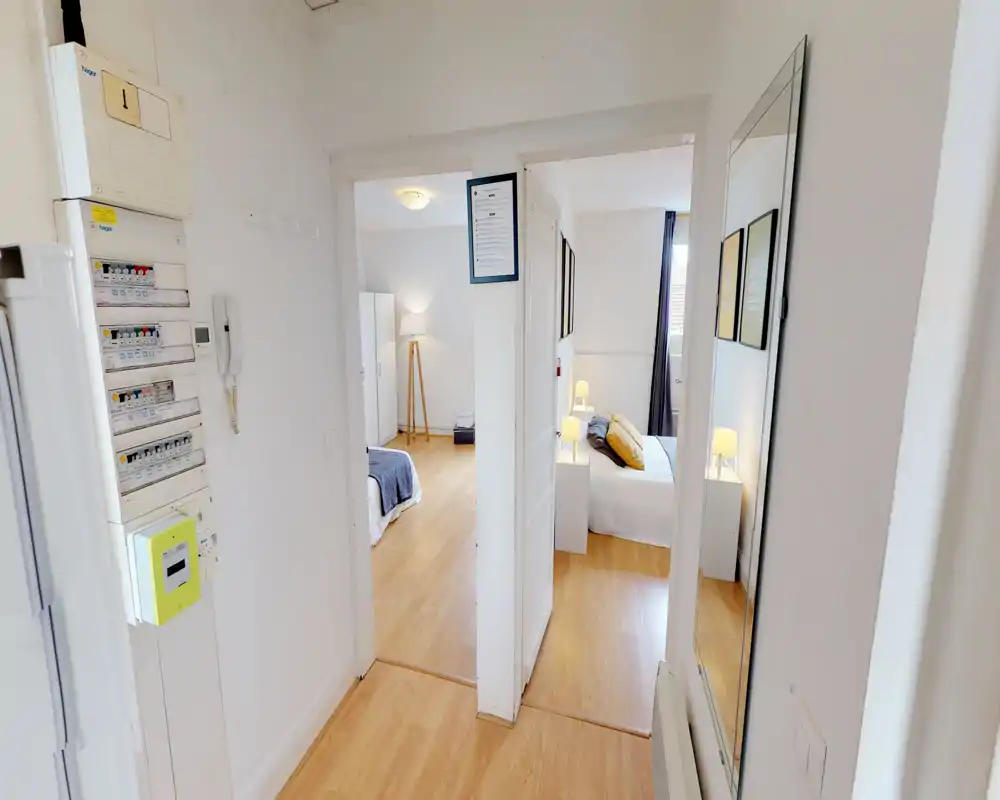 Well-staged bedroom view with a neatly made double bed, warm bedside lamps and hardwood floors; bright and inviting atmosphere ideal for rental photos.