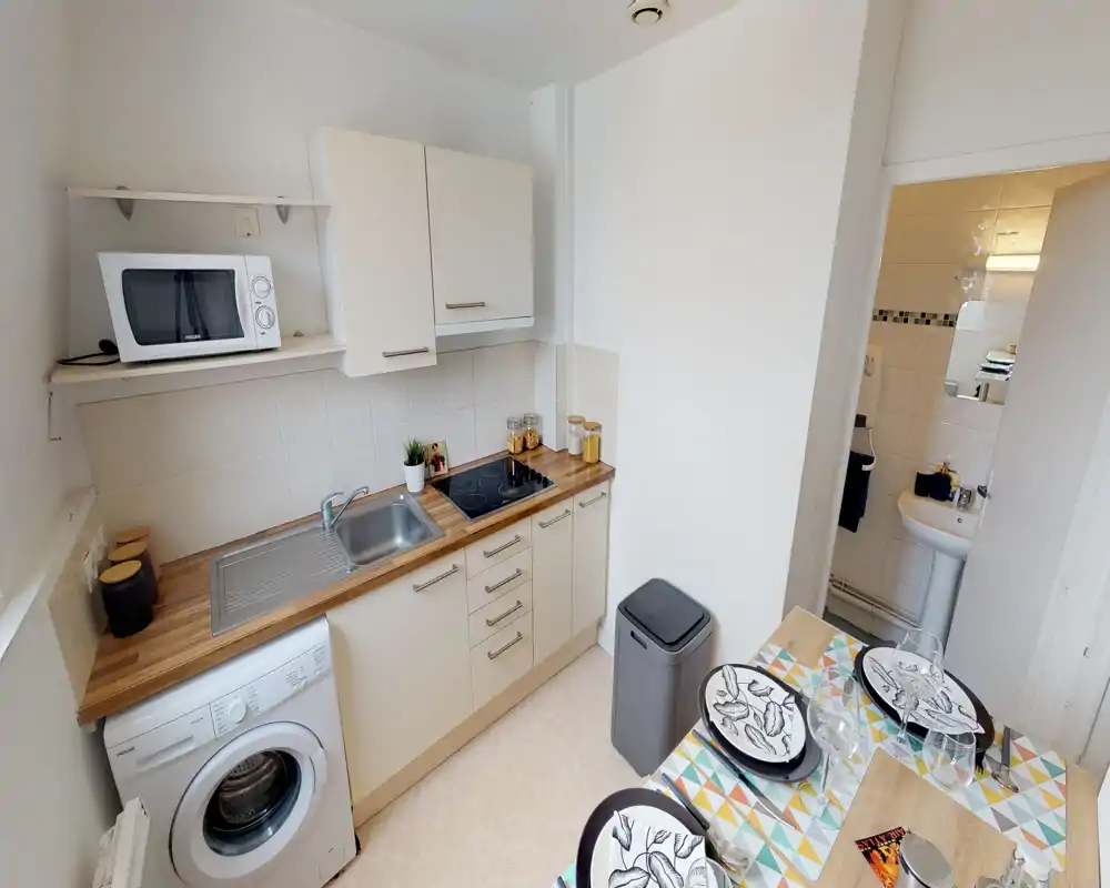 Compact, well-equipped kitchen with a wooden countertop, sink, hob and washing machine. Small decorative touches and a set dining area make it practical and inviting for a short stay.