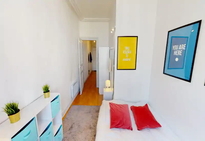 Chambre lumineuse et bien mise en scène avec lit double, coussins colorés et cadres muraux. Mobilier minimal, petite lampe de chevet et rangements, ambiance chaleureuse adaptée aux photos d’annonce.