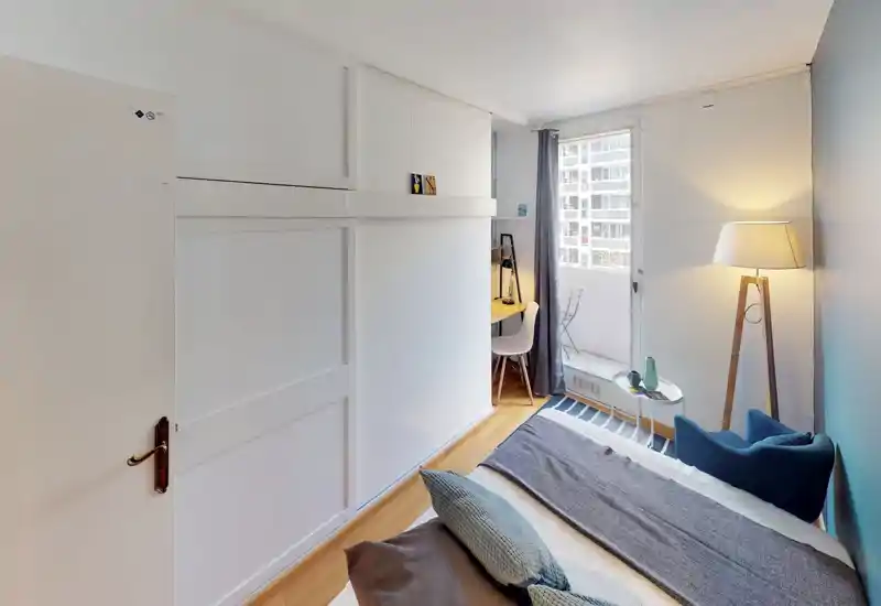 Bright, well-styled bedroom with a visible double bed, cozy textiles and a reading corner by the window. Natural light and a floor lamp create a warm, inviting atmosphere.
