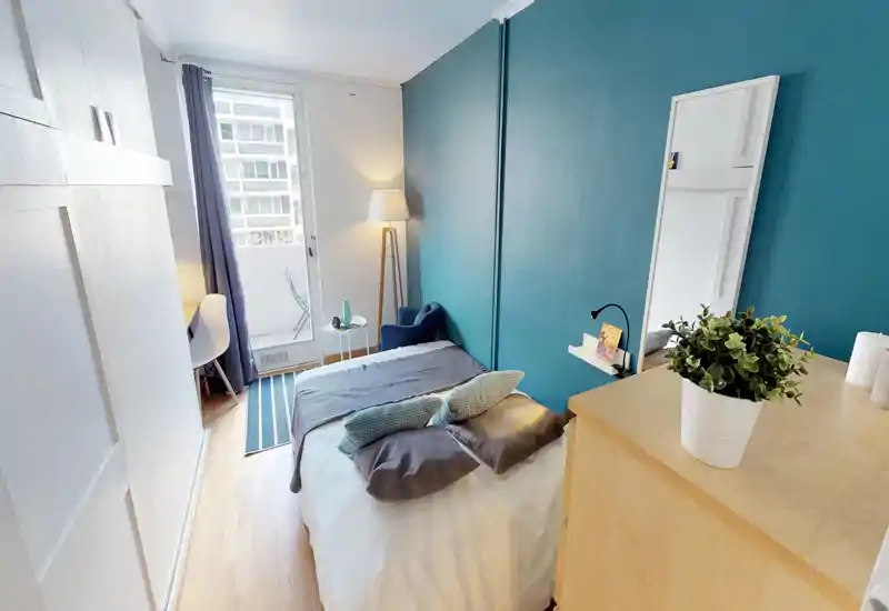 Bright, well-styled bedroom with a queen-size bed, teal accent wall, bedside lamp and a small balcony. The room feels cozy and well-lit, ideal for rental photos.