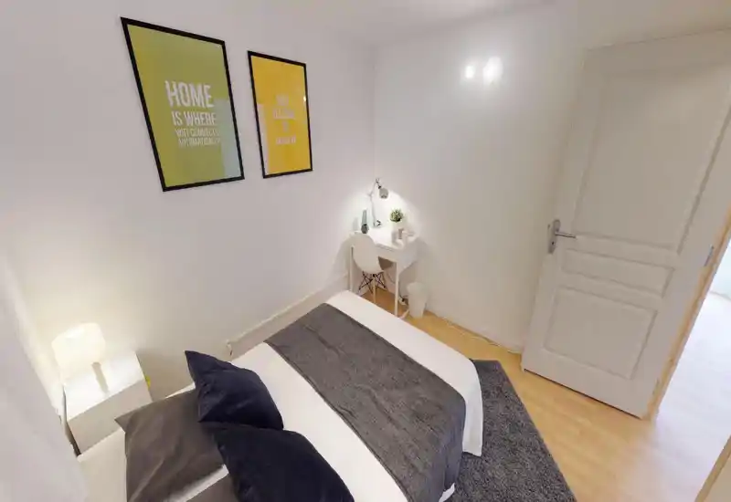 Bright, minimalist bedroom with a double bed dressed in neutral linens, bedside lamp and a small white desk with task lamp — ideal for a restful stay or light remote work.