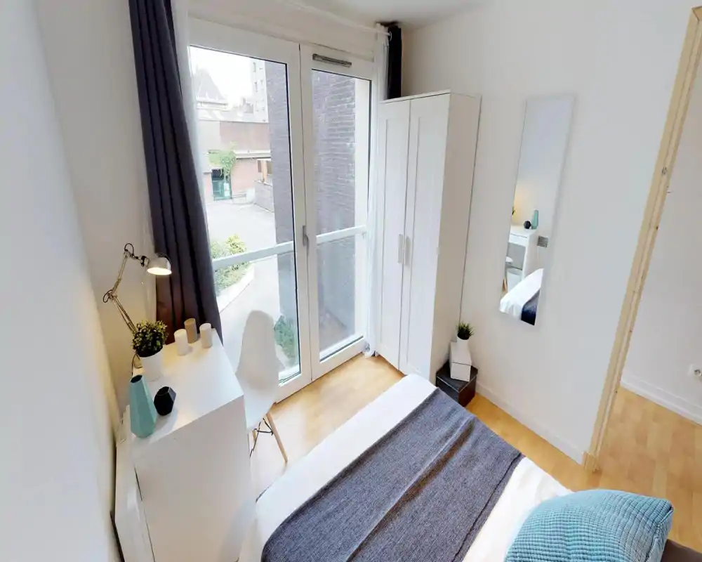 Camera da letto singola luminosa e ben arredata con letto visibile, scrivania, armadio e una grande finestra con vista sulla strada — perfetta per un affitto luminoso.