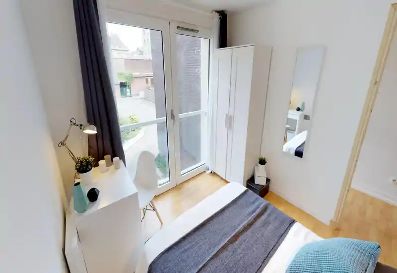 Bright, neatly styled single bedroom with a visible double bed, desk, wardrobe and large window offering street views — ideal for a well-lit rental.