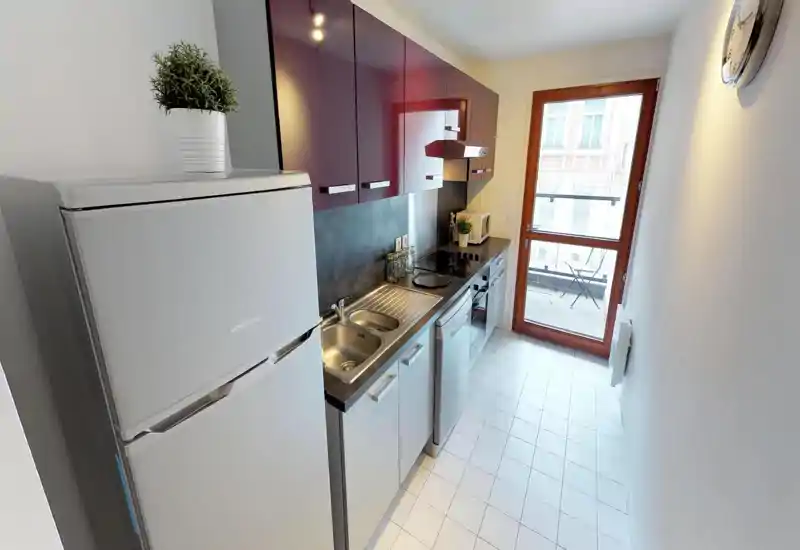 Cuisine en enfilade moderne avec placards brillants, évier en acier, plaque à induction et porte vitrée laissant entrer une belle lumière naturelle.