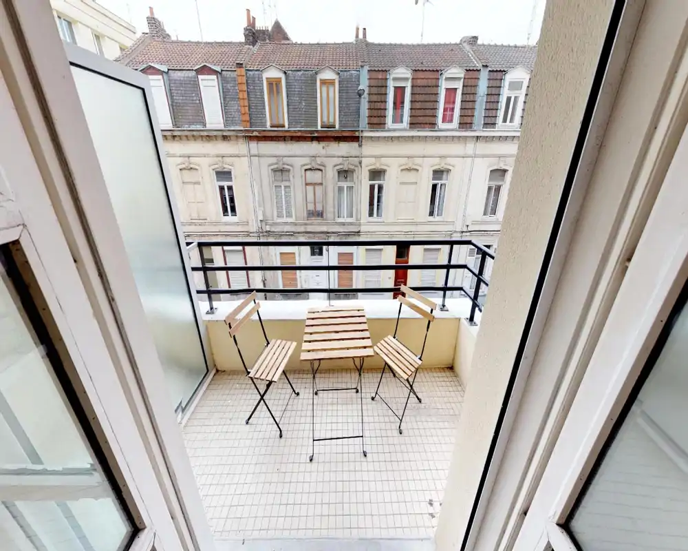 Small balcony with a bistro table and chairs overlooking classic city buildings; suitable for morning coffee despite heavy image artifacts.