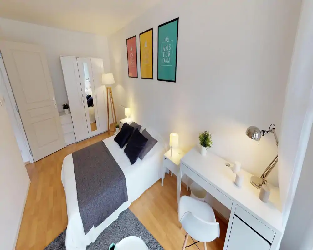 Bright, modern bedroom with a neatly made double bed, bedside tables and a white desk by the window. Clean wooden floors, framed prints over the bed and soft lighting create a calm, welcoming atmosphere ideal for listings.