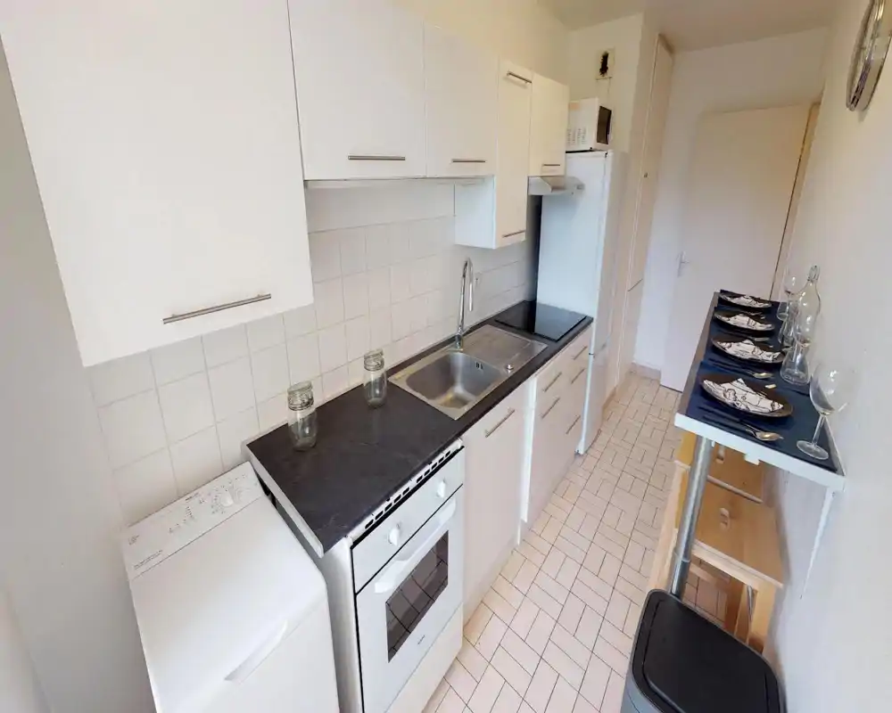 Cucina a corridoio compatta e funzionale con mobili bianchi, lavello integrato, forno e frigorifero; un piccolo bancone con posti a sedere ottimizza lo spazio.