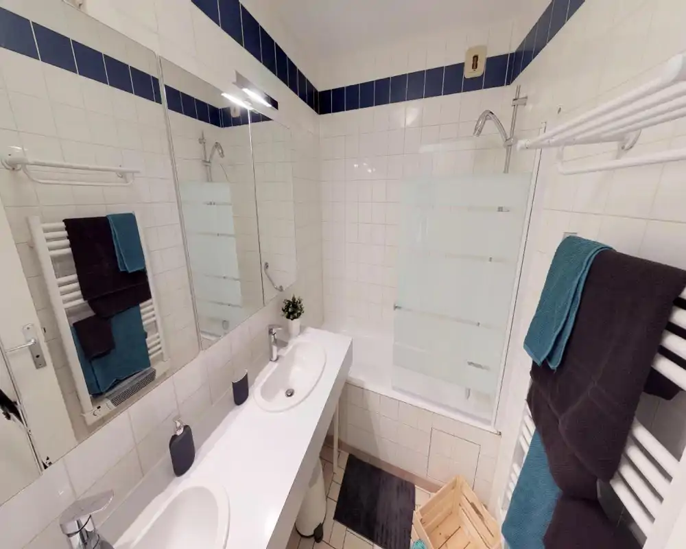 Bagno luminoso e moderno con doppio lavabo, grande specchio, vasca con paratia in vetro e scalda-asciugamani con asciugamani piegati.