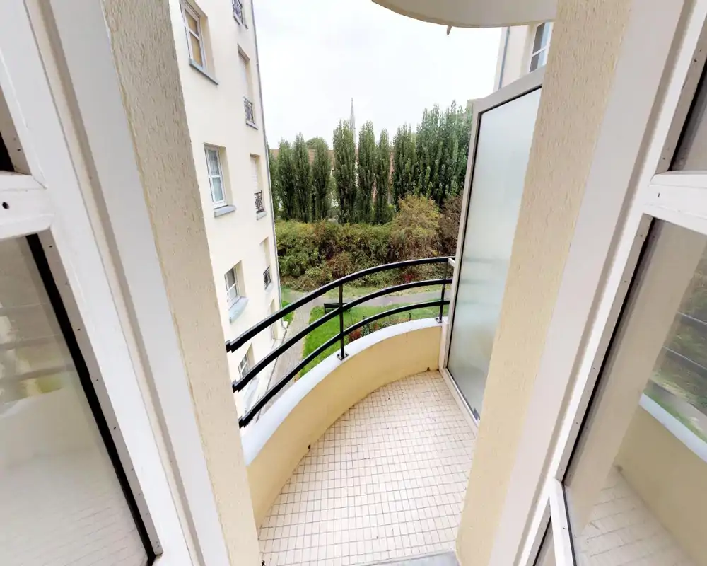 Piccolo balcone curvo con pavimento piastrellato, ringhiera in metallo e vista sul verde — ideale per un caffè mattutino o un tavolino con sedie.