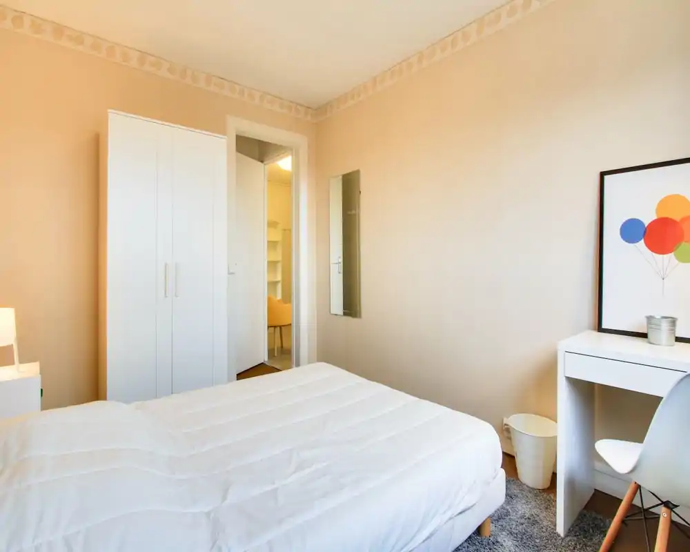 Chambre lumineuse et sobrement meublée avec lit double bien fait, armoire blanche et petit bureau — décoration chaleureuse et minimaliste, idéale pour courts séjours.