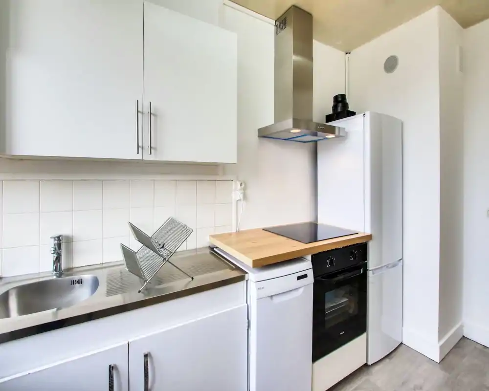 Bright compact kitchen with white cabinetry, stainless steel sink, induction cooktop and integrated appliances. Clean minimalist styling and practical countertop space ideal for a small apartment.